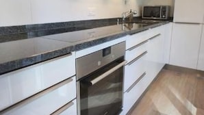 A modern kitchen with white cabinets, a granite countertop, stainless steel appliances, and a wooden floor. - Residenza San Materno Apt. 3 by Interhome (Ascona)