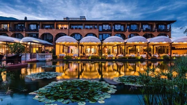 A hotel with a large outdoor pool surrounded by umbrellas, reflecting the building and sky. - Maisonettewohnung in Residenz des Giardino Ascona by Interhome (Ascona)