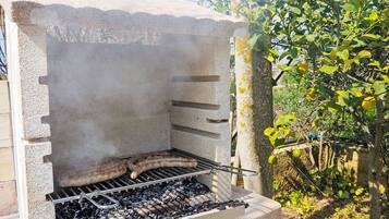Una griglia per barbecue in cemento con una griglia metallica, immersa nel verde e delimitata da una recinzione.