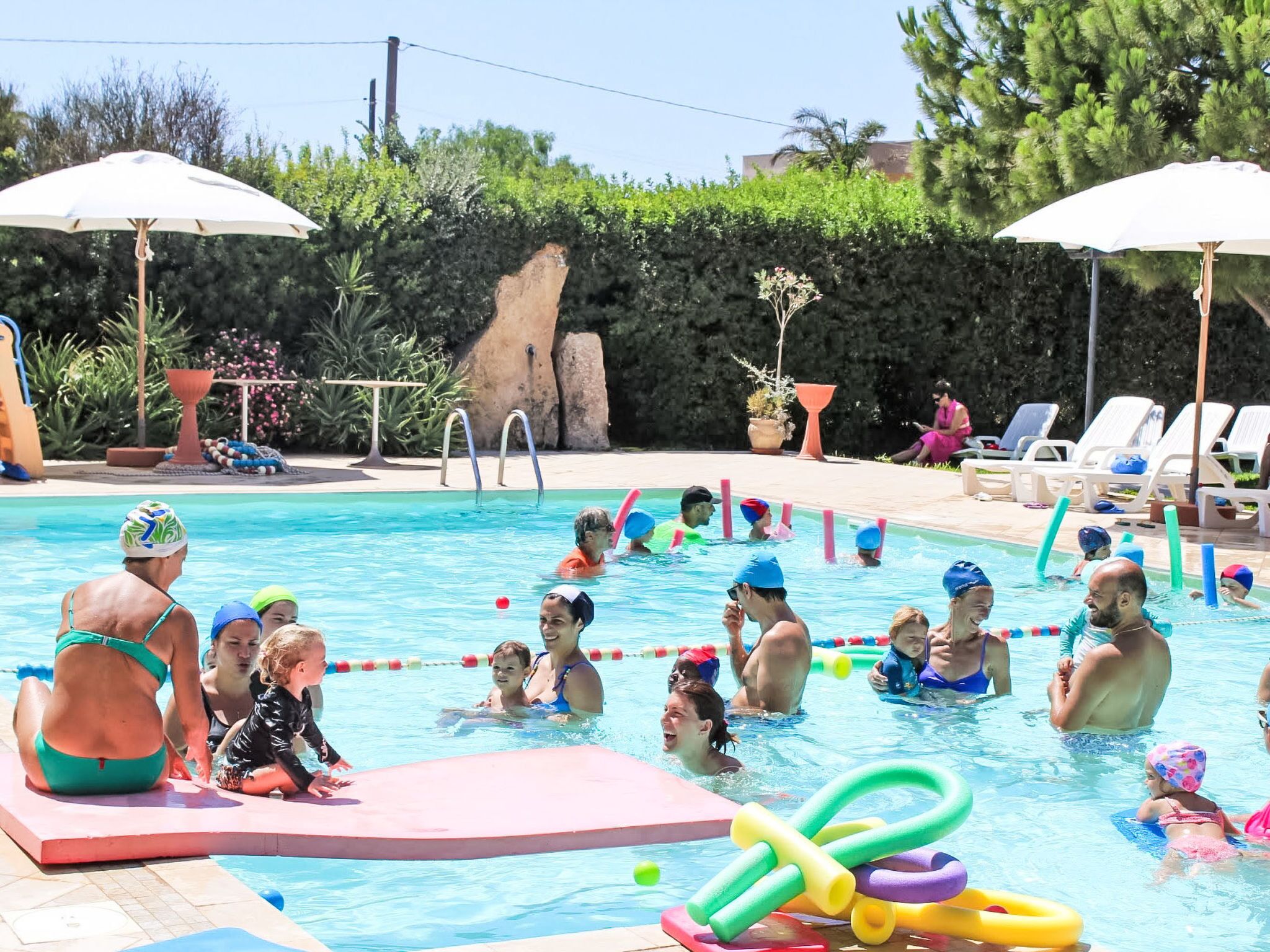 Una piscina con trampolino, sdraio e ombrelloni.
