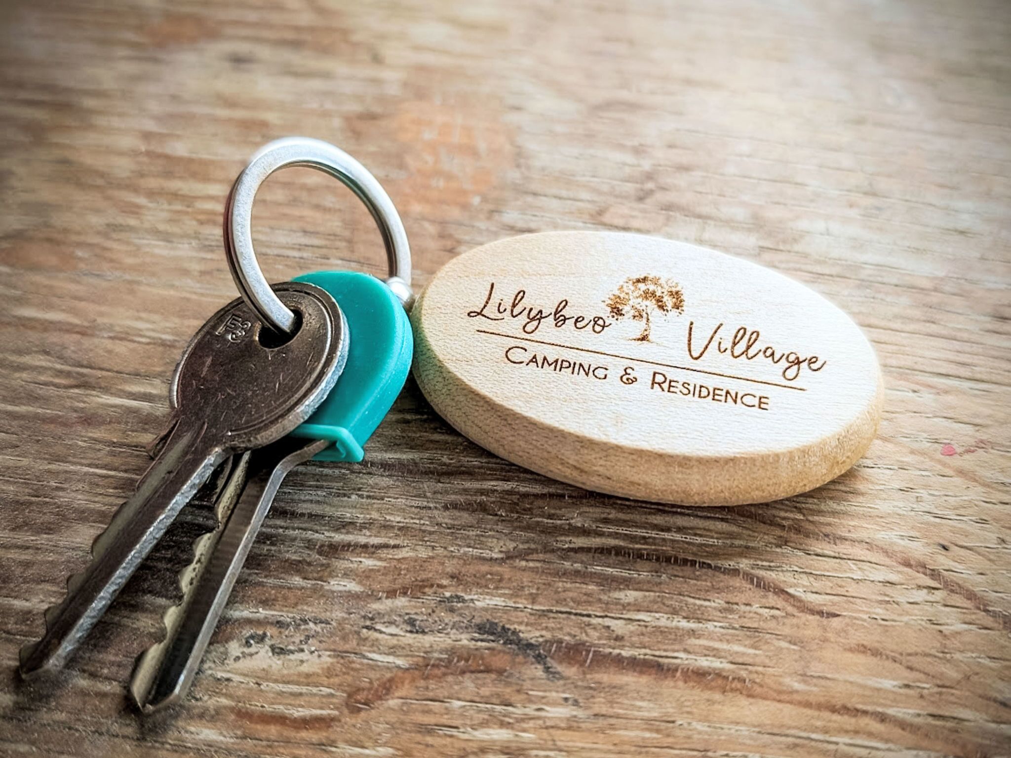 Un mazzo di chiavi con un'etichetta di legno che riporta la scritta 'Lilybee Village CAMPING & RESIDENCE'.