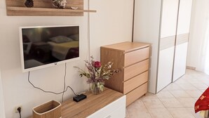 Ett modernt rum med en TV som är monterad på väggen, trähyllor med dekorativa föremål, en träbyrå och en vas med blommor på en träkonsol.
