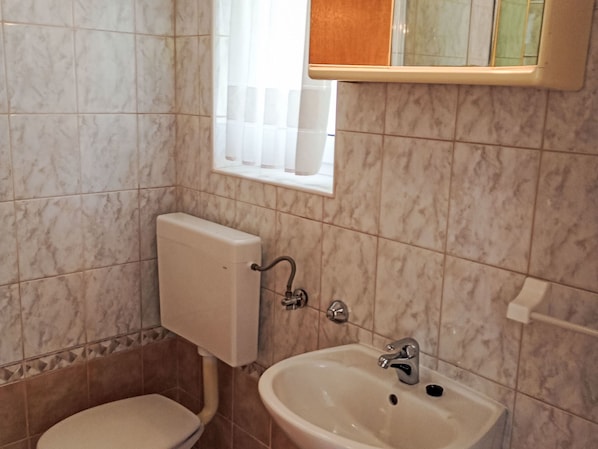 A bathroom with a toilet, sink, and window.