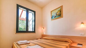 Un dormitorio con una cama, una ventana, un cuadro y una mesita de noche.