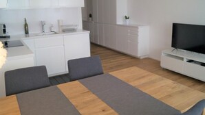 A modern kitchen with white cabinets, a dining area with a table and chairs, and a TV on a white stand. - Panorama Locarno by Interhome (Locarno)