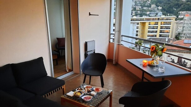 A balcony with a sofa, chairs, a table with food, and a city view. - Panorama Locarno by Interhome (Locarno)
