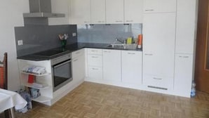 Una cucina compatta con mobili bianchi, un piano di lavoro nero e un forno integrato.
