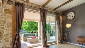 Een ruime kamer met een grote schuifdeur naar een terras, een houten vloer en een wandklok.