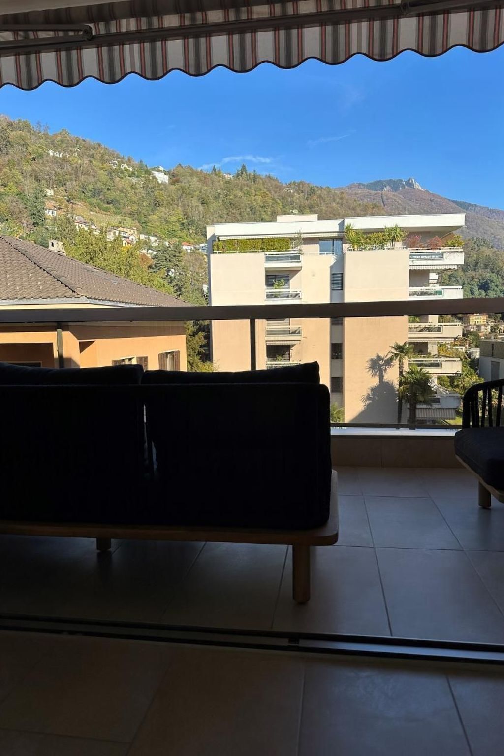 Een balkon met een bankje, uitzicht op een heuvel met gebouwen en een heldere lucht.
