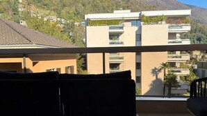 Ein Balkon mit einer Sitzbank, Blick auf eine Hügelslandschaft mit Gebäuden und einem klaren Himmel.