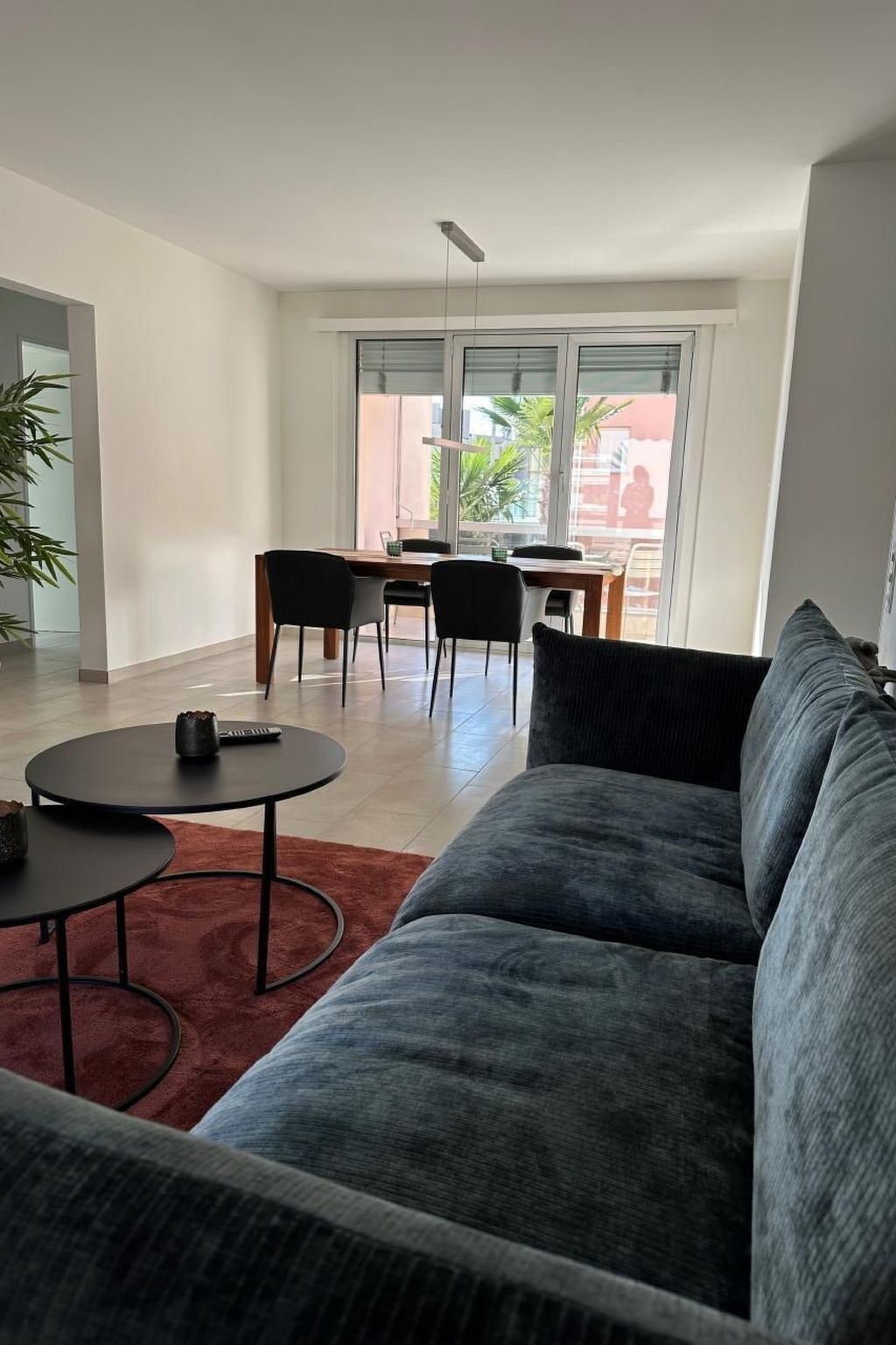 En moderne stue med en grå sofa, et rundt sofabord og et spiseområde med stole og bord.