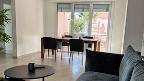 Ein modernes Wohnzimmer mit grauem Sofa, einem runden Couchtisch und einem Essbereich mit Stühlen und Tisch.