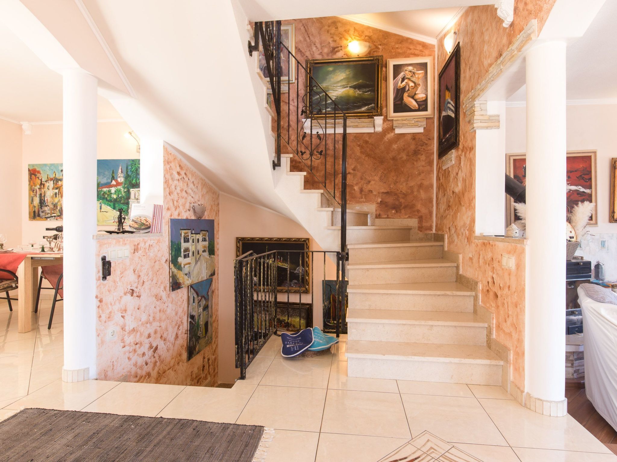A staircase with a marble finish, surrounded by artwork and a dining area with a table and chairs.