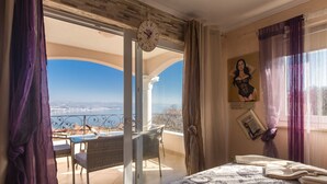 Camera da letto con un ampio letto, vista sul mare e un balcone con tavolo e sedie.