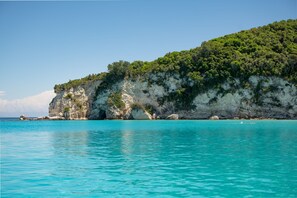 A coastal landscape with clear turquoise waters, a rocky cliff, and dense green vegetation. - Thodoros in Paxi With 3 Bedrooms and 2 Bathrooms (Paxos)