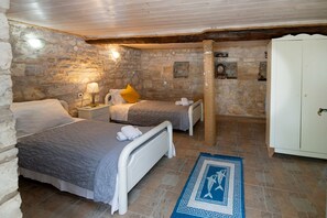 A bedroom with two beds, stone walls, a wooden ceiling, and a white wardrobe. - Thodoros in Paxi With 3 Bedrooms and 2 Bathrooms (Paxos)