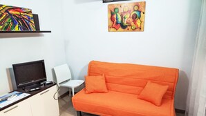 Een kamer met een bank, een televisie, een tafeltje en een stoel.