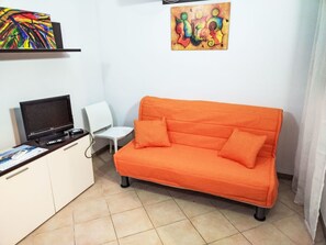 Ein Zimmer mit einer Couch, einem Fernseher, einem kleinen Tisch und einem Sessel.