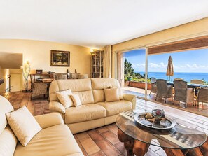 A spacious living room with a large beige sofa, a glass coffee table, and a view of the ocean through large sliding glass doors. - Bellevue by Interhome (Les Issambres)