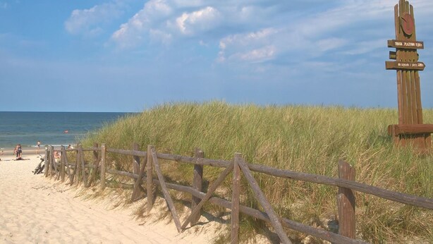 Ein Strand mit einer Holzlattenzaun und einem Wegweiser, der Entfernungen zu nahegelegenen Orten angibt.
