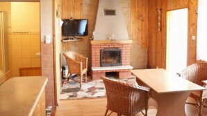Ein gemütliches Zimmer mit Kamin, Fernseher, Korbsesseln und Fliesenboden.