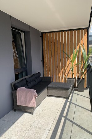 Ein moderner Außenbereich mit einer grauen Rattan-Couch, passendem Hocker und einem Holzlatten-Raumteiler.