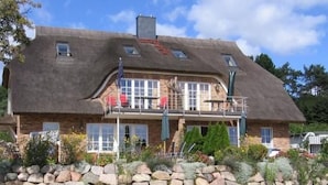 Et toetagers hus med en facade af sten, et stråtækt tag og en balkon med gelændere.