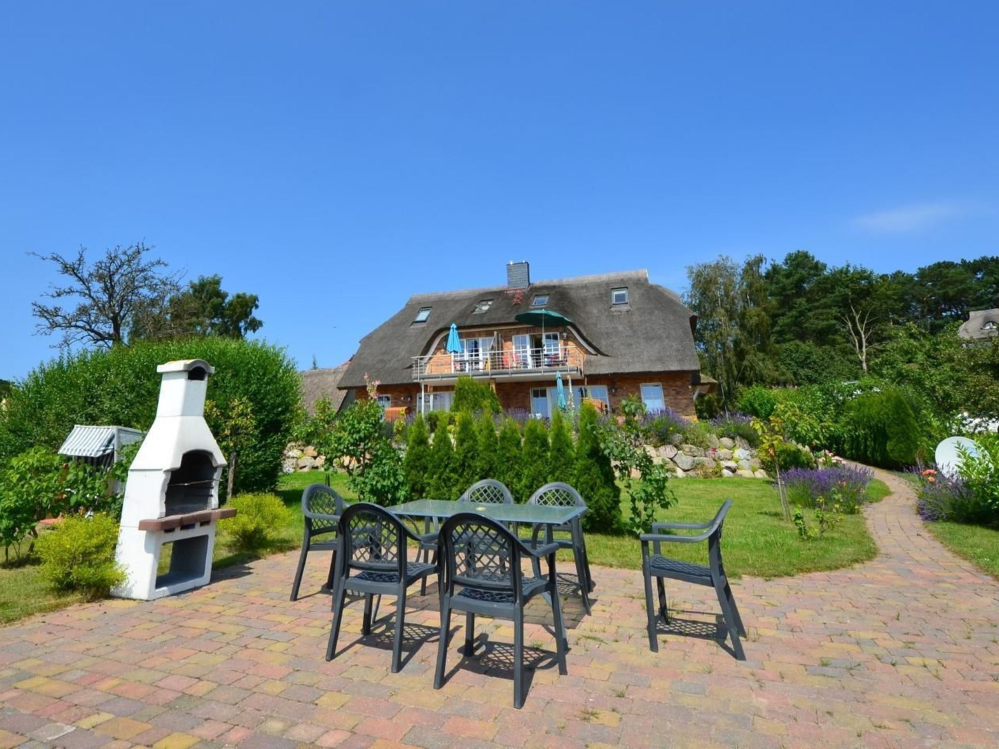Een huis met een patio, een barbecue, buitenmeubels en een tuinpad.