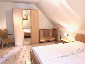 A bedroom with a single bed, a wooden crib, a wardrobe, and a chair. - Haus am Meer by Interhome (Glowe)