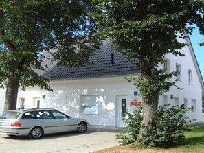 A white building with a tiled roof, a parked car, and a tree in the foreground. - Haus am Meer by Interhome (Glowe)