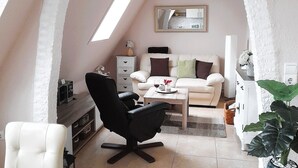 A cozy loft apartment with a high ceiling, a white sofa, a black office chair, a small dining table, and a large window. - Geräumige Ferienwohnung in Zingst mit Terrasse by Interhome (Ostseebad Zingst)