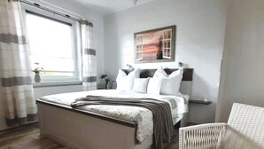 A bedroom with a large bed, a chair, a painting on the wall, and a window with curtains. - Geräumige Ferienwohnung in Zingst mit Terrasse by Interhome (Ostseebad Zingst)