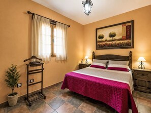 A bedroom with a bed, two bedside tables, a nightstand, a hanging lamp, a window with curtains, a wall-mounted painting, and a plant. - "La Almendra" mit Terrasse by Interhome (San Bartolomé de Tirajana)