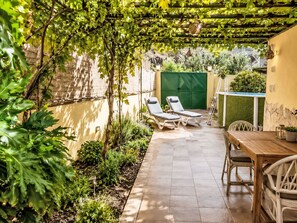 Um pátio coberto com duas cadeiras de descanso, uma mesa e uma pequena área de piscina.