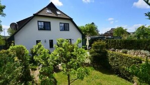 A white house with a tiled roof, surrounded by a well-maintained garden with various shrubs and a small tree. - Haus Komoran by Interhome (Baabe)