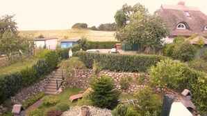 A garden with a stone bench, a small pond, and a thatched-roof house. - Haus Komoran by Interhome (Baabe)