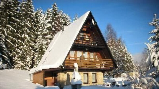 Eine Holzhütte mit steilem Dach, umgeben von schneebedeckten Bäumen.