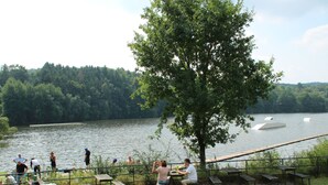 Area picnic sul lago con panche e tavoli di legno, circondata da una recinzione in metallo.