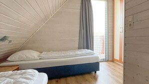 Camera da letto con soffitto a falde, un letto, una finestra con tende e una porta che dà su un balcone esterno.