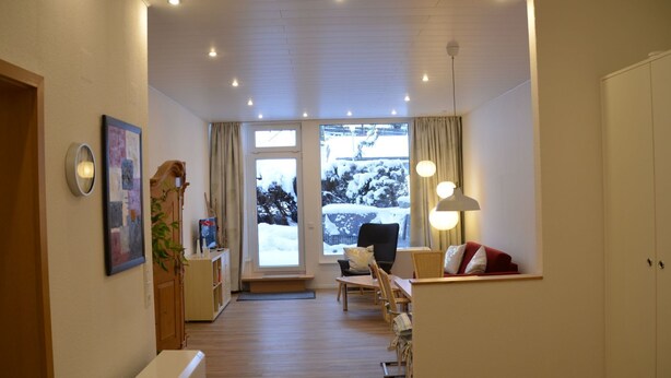 Un salon moderne avec un plancher en bois, un canapé, une table à manger et une grande fenêtre donnant sur des arbres couverts de neige.