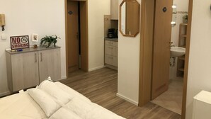 Une chambre d’hôtel avec un lit, un bureau sur lequel est posé un panneau « Interdiction de fumer », un miroir et une salle de bain visible à travers une porte ouverte.
