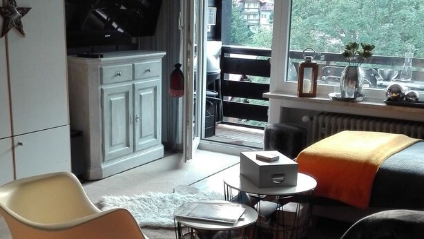 Un salon moderne avec un piano, un canapé, une table basse et une vue sur un balcon doté d’une balustrade et de plantes vertes.