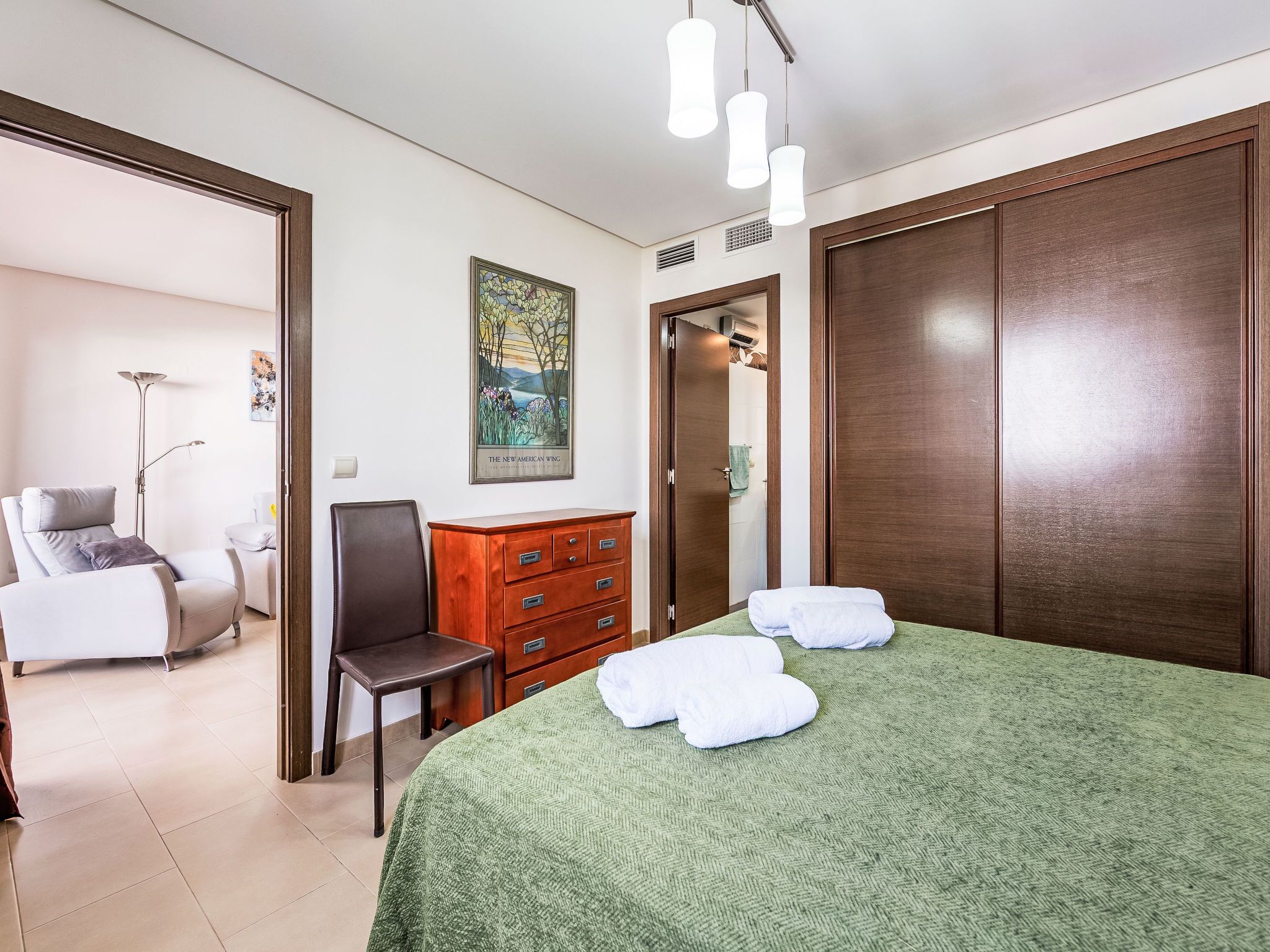 A hotel room with a bed, a chair, a dresser, a painting, and a wardrobe.