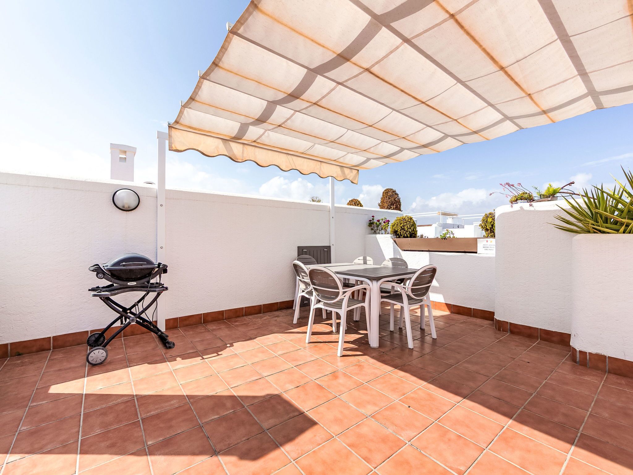 Un pati amb una barbacoa, taula exterior, cadires i una paret blanca.