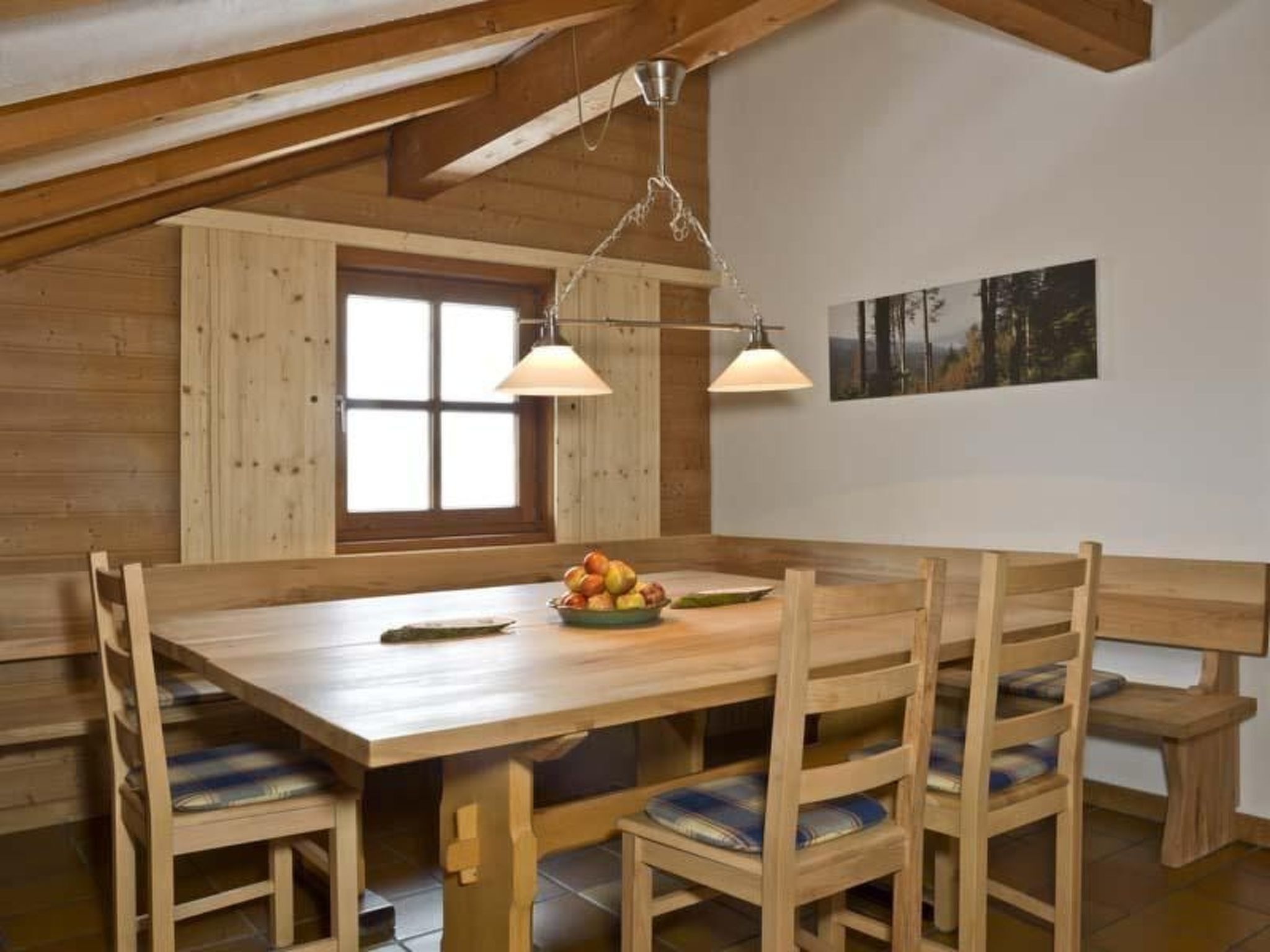 Un coin repas en bois avec une grande table, des bancs et un luminaire suspendu.