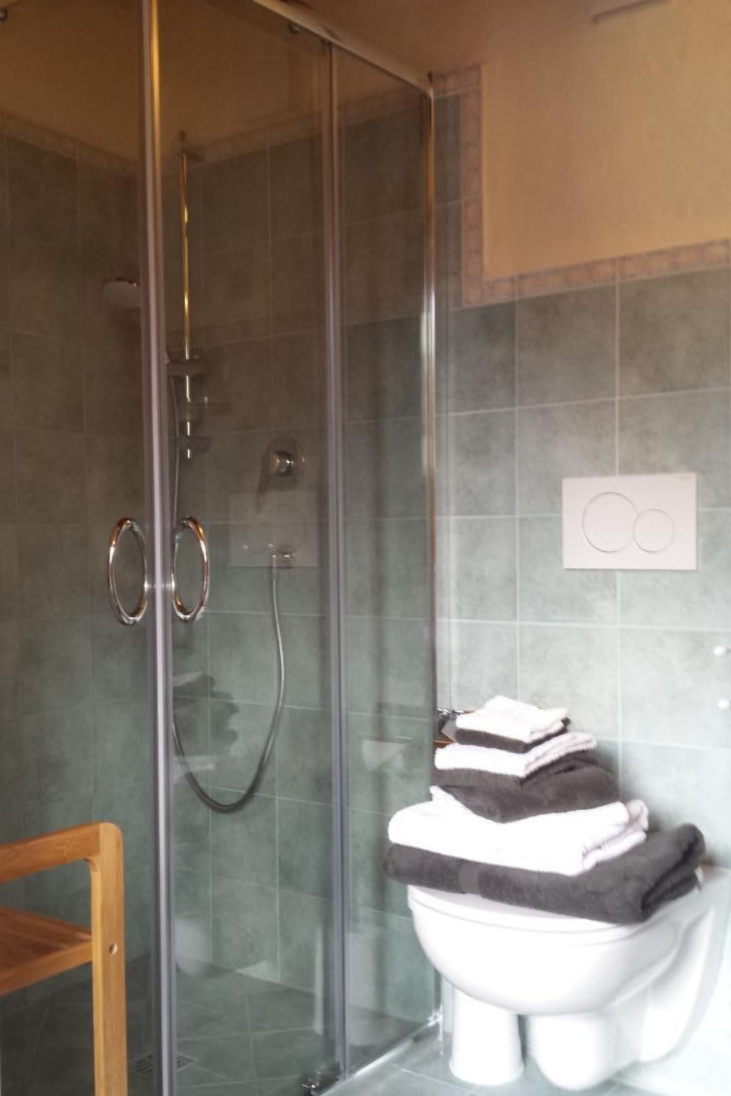Une salle de bain avec une douche à parois de verre, des toilettes avec une pile de serviettes à proximité, et un interrupteur fixé au mur.