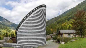 Ein einzigartiges, zylindrisches Gebäude mit gewölbter Dachkonstruktion, eingebettet in eine ländliche Landschaft mit Bergen und traditionellen Häusern.