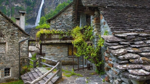 Ein rustikales Steinhaus mit einem Holzbalkon und einer Steintreppe, die zu einer Tür führt.