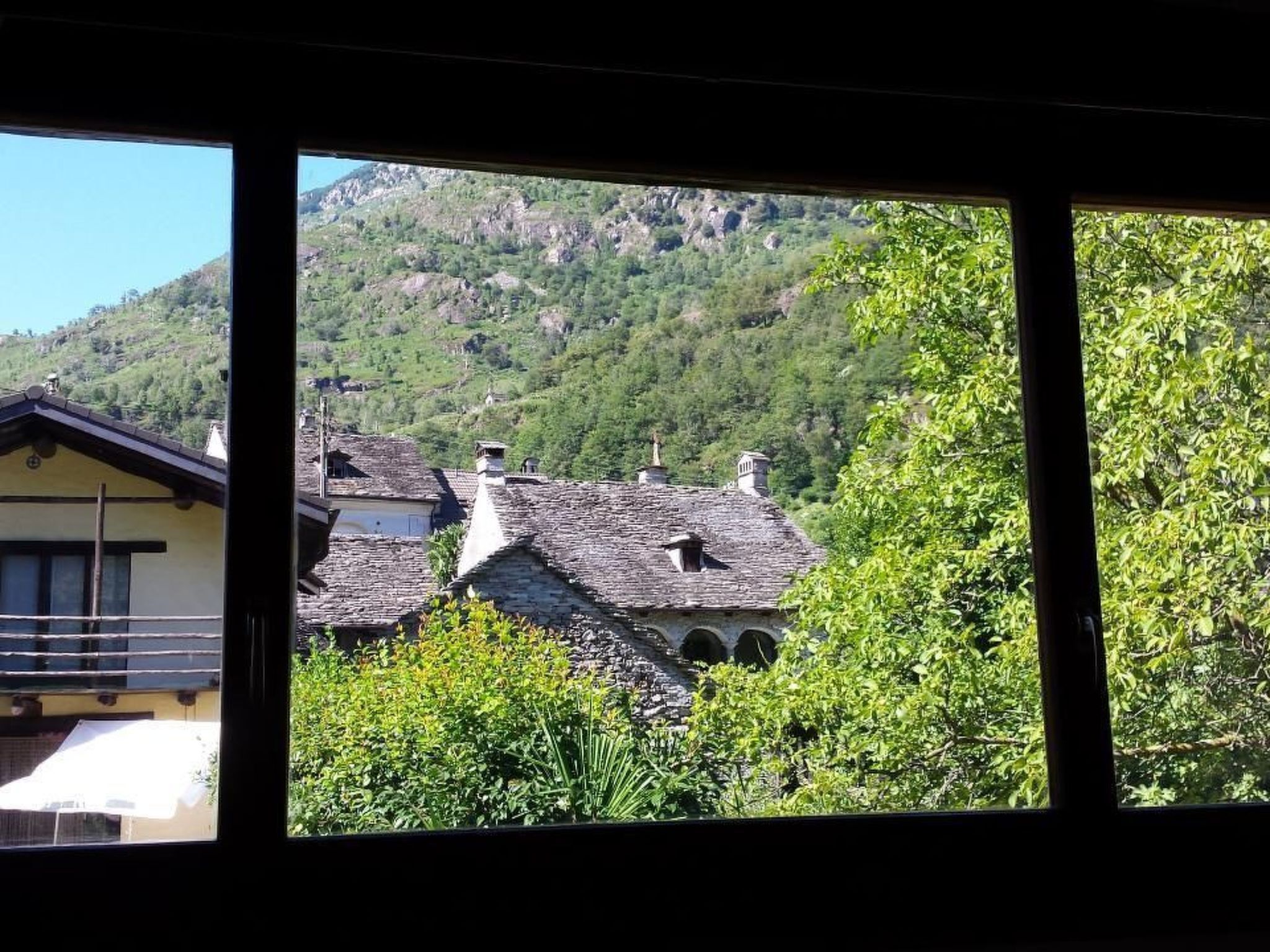 Vista de un paisaje montañoso con edificaciones tradicionales, incluyendo una casa con techo inclinado y un edificio de piedra con múltiples chimeneas.