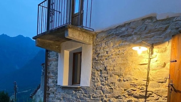 Un edificio in pietra con un balcone, un tavolo e panche, e vista sulle montagne.